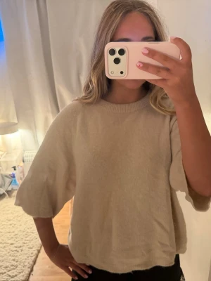 Beige oversized stickad tröja - Mysig beige stickad tröja med breda, halvlånga ärmar och avslappnad passform. Tröjan har ribbad halsringning och är gjord i ett mjukt material som känns skönt mot huden. Perfekt för en chill och stilren look.