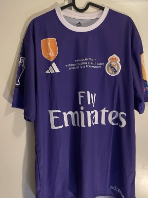 Lila Real Madrid Ronaldo tröja - Cristiano Ronaldo x Real Madrid från Champions League-finalen 2018 i Kyiv. En klassisk och eftertraktad design i lila.  * Helt ny och oanvänd * CR7 på ryggen * Real Madrid 2018 * UCL Final Kyiv * Bra material och fin passform * Ligger kvar i paket  Perfekt för dig som är CR7- eller Real Madrid-fan, eller för samlingen.
