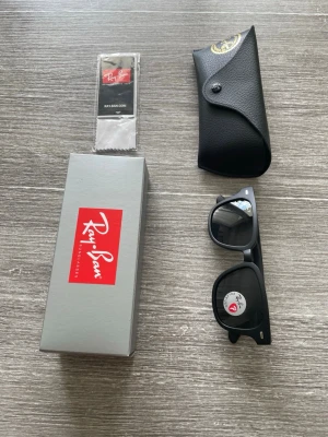 Svarta Ray-Ban solglasögon Wayfarer - Säljer ett par klassiska svarta Ray-Ban Wayfarer solglasögon med polariserade linser. Snygg och tidlös design med mattsvart båge i plast. Kommer med originalfodral, putsduk och box. Perfekta för soliga dagar och ger en clean look.