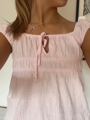 Ljusrosa blus - Supersöt ljusrosa blus med korta ärmar och knytdetalj vid halsen. Kan bäras på olika sätt!💕