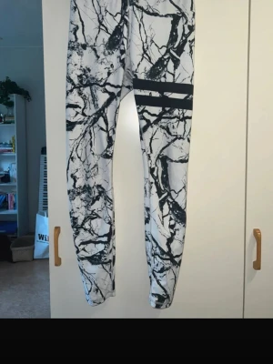 Vita leggings med svart marmorprint - Snygga vita leggings med svart marmorliknande mönster och två svarta ränder på låret. Tight passform och stretchigt material som passar perfekt till träning eller chill. Hög midja för extra komfort.