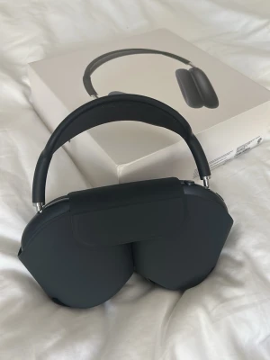 Svarta AirPods Max - Snygga svarta over-ear hörlurar med stilren design och mjuka öronkuddar. Bågen är vadderad och har mesh-tyg på insidan för extra komfort. Hörlurarna har en modern look och levereras med originalförpackning.