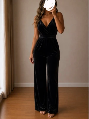 Svart sammetsjumpsuit med v-ringning - Supersnygg svart jumpsuit i mjuk sammet med djup v-ringning och breda axelband. Markerad midja och vida ben ger en riktigt trendig siluett. Perfekt för dig som vill sticka ut med en elegant och bekväm look.
