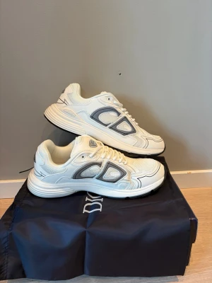 Vita sneakers  - Snygga vita sneakers med grå och svarta detaljer. Skorna har en chunky sula och meshpaneler för extra komfort och stil. Perfekta för dig som gillar en sportig och modern look. Klassisk låg modell med tydlig ogga på sidan.