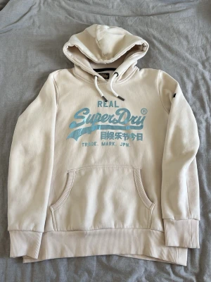 hör gärna av er om ni har några frågor - En beige superdry hoodie med ljusblått tryck