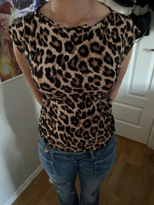 Leopardmönstrad topp med kort ärm - Snygg topp med leopardmönster i beige och svart. Modellen har korta ärmar och rund halsringning. Perfekt för dig som vill sticka ut med ett djuriskt print. Materialet känns mjukt och följsamt mot kroppen.