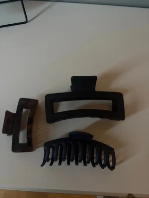 Set med tre hårklämmor - Säljer ett set med tre hårklämmor i olika former och färger. En är svart och rektangulär, en är mörkbrun med sköldpaddsmönster och en är svart med rundad form. Perfekta för att snabbt sätta upp håret och skapa snygga frisyrer.