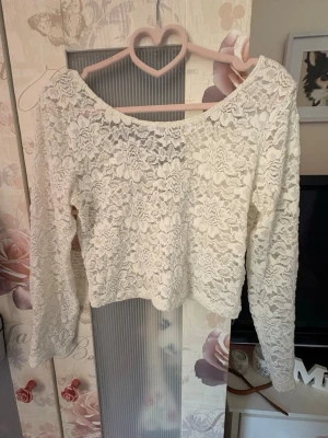 Vit spetsblus från H&M Divided - Säljer en vit långärmad spetsblus från H&M Divided. Blusen har ett blommigt spetsmönster, är croppad och har en bred, något offshoulder ringning. Perfekt för dig som gillar romantisk och trendig stil.