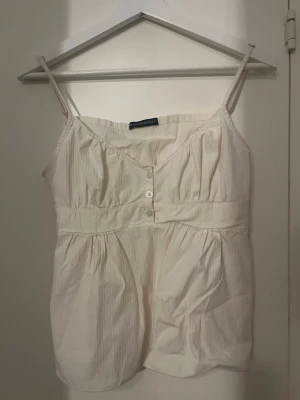 Vit topp med knappar - Söt cream vit  topp med tunna axelband som går att  justera och knappar framtill. Smock i ryggen för en bekväm passform. Perfekt för varma dagar och enkel att styla med jeans eller kjol. I storlek S, jag köpte den här på Plick men den var för liten. Pris går att diskutera🌸