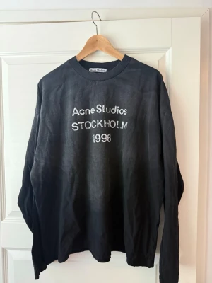 Acne studio sleeve svart - Cool svart långärmad tröja från Acne Studios med vit text 'Acne Studios STOCKHOLM 1996' på bröstet. Tröjan har rund halsringning och avslappnad passform, perfekt för en trendig streetwear-look.