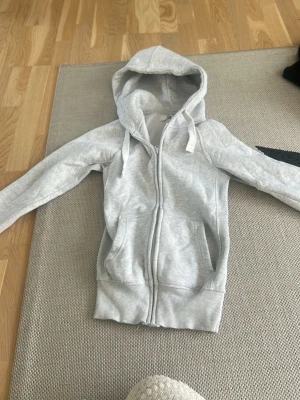 Ljusgrå zip hoodie med huva - Snygg ljusgrå hoodie med dragkedja framtill och två fickor. Tröjan har en klassisk huva med dragsko och ribbade muddar vid ärmslut och nederkant. Perfekt för en avslappnad och chill stil. Materialet känns mjukt och bekvämt. I stl Xxs