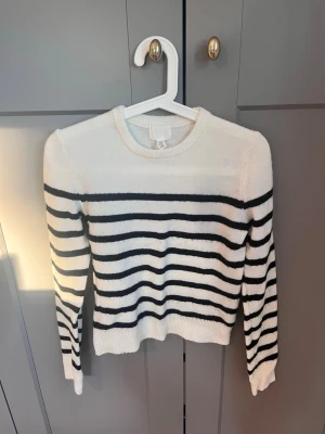 Vit stickad tröja med svarta ränder - Vit stickad tröja från H&M med svarta horisontella ränder. Tröjan har rund halsringning, långa ärmar och ribbade muddar vid ärmslut och nederkant. Perfekt för en avslappnad och trendig look.