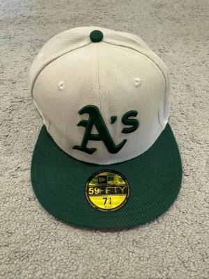 Oakland A's 59FIFTY keps grön/vit - Snygg 59FIFTY keps från New Era med Oakland A's logga framtill. Kepsen är vit med grön skärm och gröna detaljer. På sidan finns ett broderat 1989 World Series-märke. Perfekt för dig som gillar baseball eller streetwear.
