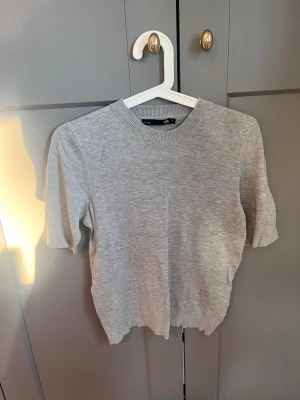 Grå ribbad topp  - Säljer en enkel och stilren grå topp från 157 med ribbad rund hals och korta ärmar. Perfekt till jeans eller kjol och lätt att matcha med andra plagg. Materialet känns mjukt och bekvämt mot huden.