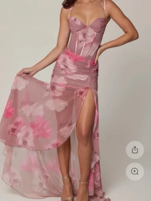 Lång blommig rosa klänning - Romantisk långklänning med blommigt mönster i rosa och röda toner. Klänningen har smala axelband, markerad byst och draperade detaljer i midjan. Tillverkad i ett lätt, flytande material som ger en elegant siluett.