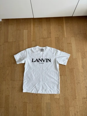 Lanvin T-shirt - Säljer en vit t-shirt från Lanvin x Gallery Dept. med stor svart logga på bröstet. Klassisk rund hals och korta ärmar. Perfekt för dig som gillar stilrena plagg med tydlig branding.
