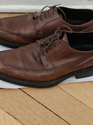 Bruna loafers i läder från playboy 41 - Snygga bruna loafers i äkta läder med klassisk design och svarta sulor. Skorna har dekorativa sömmar och snörning framtill för en stilren look. Perfekta för dig som vill ha ett par tidlösa och mångsidiga skor till garderoben. 41 i storlek men känns även upp mot 42 . 