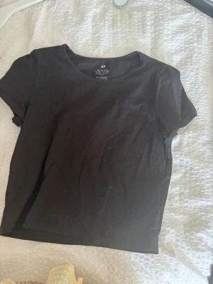 Svart basic t-shirt från H&M - En enkel svart t-shirt från H&M i mjuk bomull. Klassisk rund halsringning och korta ärmar. Perfekt till jeans eller shorts för en clean och avslappnad look.