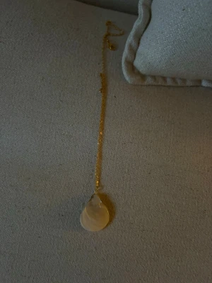 Guldhalsband med snäcka  - Snyggt halsband med tunn guldfärgad kedja och en stor droppformad pärla som hänge. Perfekt för dig som gillar stilrena och eleganta accessoarer med en naturlig touch. Lätt att matcha med olika outfits.