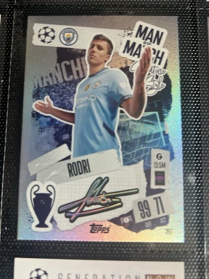 Manchester City Rodri samlarkort - Samlarkort från Topps med Rodri i Manchester Citys ljusblå matchtröja. Kortet har holografisk yta, texten 'Man of the Match' och Rodris autograftryck. UEFA Champions League-logga och statistik finns med på framsidan. KAN DISKUTERA PRIS