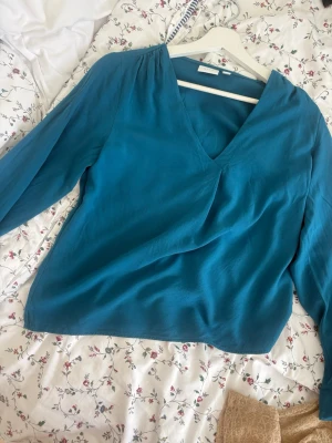 Blå omlottblus från VILA - Snygg blå omlottblus från VILA med v-ringning och långa ärmar. Tillverkad i ett mjukt, lätt material som ger ett fint fall. Perfekt att styla med jeans eller kjol för en trendig look.