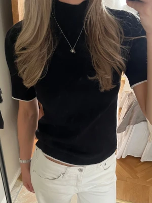Svart polotopp med vita detaljer - Snygg svart polotopp med korta ärmar och vita kontrastkanter vid ärmslut och hals. 