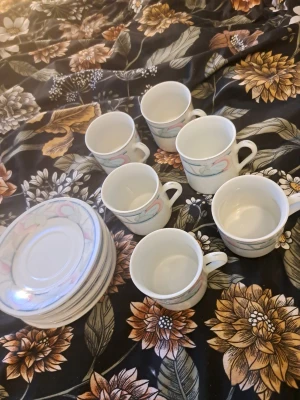 Kaffekopp med fat, pastellmönster - Säljer ett servis-set bestående av 6 koppar och 6 fat i porslin med ett stilrent blommönster i dämpade färger. Perfekt för dig som vill komplettera din servis eller ha fina koppar till kaffe eller  - 6 koppar och 6 fat - Material: Porslin - Mönster: Blommönster i ljusa pastellfärger - I gott skick utan synliga skador eller nagg - Kakfatens undersida märkt med tillverkarens stämpel (se bild) - Passar både vardagsbruk och festliga tillfällen Setet säljs komplett som en helhet.