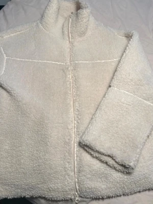 Vit teddyjacka från Gina Tricot - Mysig vit teddyjacka från Gina Tricot med dragkedja framtill och hög krage. Jackan har en fluffig. 