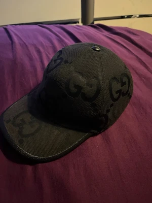Gucci Jumbo svart keps - Snygg svart keps från märket Gucci. Just denna modellen heter Jumbo. Justerbar baktill för perfekt passform. Perfekt för dig som gillar streetwear och vill sticka ut. Självklart är kepsen äkta och påse, låda, tygpåse för kepsen och kvitto fås med. 