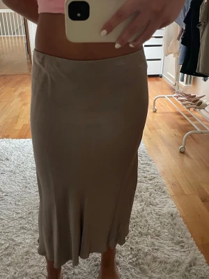 Satinkjol - Säljer en kjol i satinliknande material i brons/brun. Kjolen har en rak, figurnära passform och faller snyggt. Lite nopprig efter tvätt men går bort lätt med roller!!