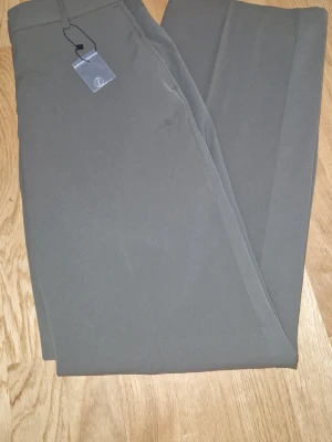 Olivgröna raka kostymbyxor - Snygga olivgröna kostymbyxor med rak passform och klassisk midja. Byxorna har pressveck och är tillverkade i ett slätt tyg som ger en stilren look. Perfekta för dig som vill ha en clean och modern stil.pris går diskutera 