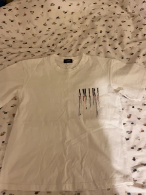 Vit t-shirt med tryck - Säljer en vit t-shirt med ett coolt tryck på bröstet där loggan droppar i svart, blått och orange. T-shirten har rund hals och korta ärmar. Perfekt för dig som gillar streetwear och vill sticka ut lite extra.