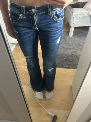Mörkblå bootcut jeans med slitningar - Säljer ett par skit snygga mörkblå lågmidjade bootcut jeans med några slitningar och detaljer på fickorna, man kan även justera de i midjan, inga defekter, nypris 399kr💕