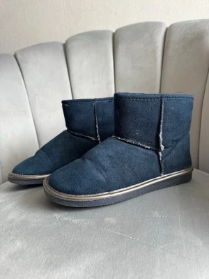 Mörkblåa mjuka skor - Ett par mörkblåa skori mockaimitation med kort skaft och synliga sömmar. De har en mjuk och bekväm sula, perfekta för att mysa runt hemma. Klassisk design med enkel form och neutrala färger som passar till det mesta.