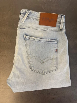 Ljusblå Replay jeans, stl 33/32 - Snygga ljusblå jeans från Replay med raka ben och klassisk femficksmodell. Jeansen har en läderpatch med Replay-logga bak i midjan och subtila slitningar framtill. Tillverkade i mjuk denim som ger en avslappnad look.