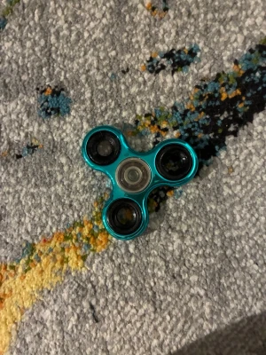 Blå metallic fidget spinner - En blå metallic fidget spinner med tre svarta kullager och rund form. Perfekt för att hålla händerna sysselsatta eller för att slappna av. Tillverkad i plast och metall.