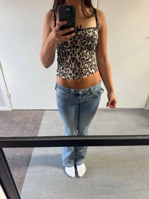 Leopardmönstrad linnetopp med rosett - Säljer en leopardmönstrad linnetopp med tunna axelband och en liten svart rosett framtill. Toppen har en beige bas med svarta och bruna leopardfläckar. Perfekt för dig som vill sticka ut lite extra.