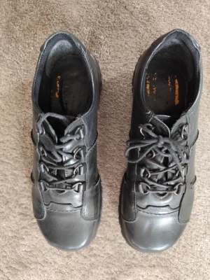 Svarta loafers i läder - Säljer ett par svarta loafers med snörning i mjukt läder. Skorna har en sportig design med robust sula och dekorativa sömmar på sidan. Passar perfekt till dig som gillar en stilren och bekväm look.