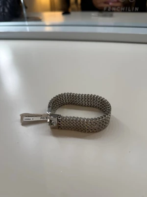 Silvrigt mesharmband i metall - Stilrent armband i silvrig metall med meshdesign som ger en modern och trendig känsla. Armbandet har en rektangulär form och ett smidigt spänne. Perfekt accessoar för att lyfta din outfit med en cool detalj. Storlek S, från Edblad 