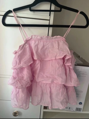 🩷 Gina Tricot rosa volanglinne | 146/152 (passar XXS/XS) - Säljer ett supersött rosa volanglinne från Gina Tricot. Märkt 146/152, men passar även XXS/XS beroende på önskad passform. Det har fina volangdetaljer och är perfekt till sommaren eller att styla med jeans, kjol eller shorts.