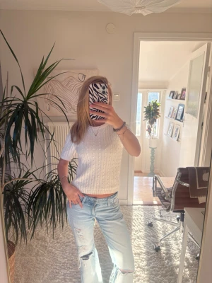 Vit kabel stickad topp - Säljer en vit, kabel stickad topp med korta ärmar och rund hals. Toppen har ett klassiskt kabelstickat mönster och är croppad i modellen. Perfekt att styla med jeans eller kjol för en clean och fräsch look. Storlek xs, ginatricot 
