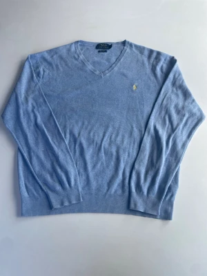 Ljusblå tröja från Polo Ralph Lauren - Snygg ljusblå tröja från Polo Ralph Lauren i mjuk pima bomull. Tröjan har två små vita fläckar på insidan/bak på högra ärmen. Se bild 4.