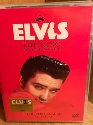 Elvis The King of Rock 'N' Roll DVD - DVD med Elvis Presley, The King of Rock 'N' Roll. Innehåller 30 hitframträdanden från TV, filmer och konserter mellan 1956 och 1970-talet. Omslaget är rött med Elvis porträtt och text i vitt och guld. Perfekt för dig som gillar klassisk rock'n'roll och musiknostalgi.