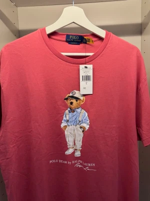 Ralph Lauren Tshirt ”Nalle trycket” - Säljer en riktigt sjyst ny oanvänd tshirt från Ralph Lauren med klassiska björn trycket, i en riktigt fin lax rosa färg. Köpt på volt för 1495. Storlek Large men storleken är som en lite större medium. KAN GÅ NER I PRIS VID SNABB AFFÄR! ™️