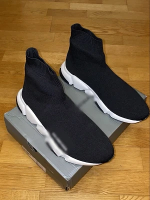 Svarta sock sneakers med vit sula - Säljer ett par svarta sock sneakers med stretchig stickad ovandel och chunky vit sula. Skorna har en strumpliknande passform som sitter tajt runt ankeln och ger en modern look. Perfekta för dig som gillar streetwear och vill ha något bekvämt och stilrent.
