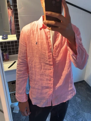 Polo Ralph Lauren skjorta  - Säljer en ljusrosa skjorta från Polo Ralph Lauren i svalt linne. Storlek L men passar M. Skjortan har klassisk krage, knappar framtill och den ikoniska loggan broderad på bröstet. Perfekt för dig som vill ha en stilren och avslappnad look. Pris kan diskuteras:)