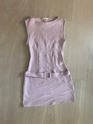 Ljusrosa ärmlös miniklänning med bälte - Säljer en ljusrosa, ärmlös miniklänning med rund halsringning och ett matchande tygbälte i midjan. Klänningen har en figurnära passform och är sydd i ett mjukt, stretchigt material. Perfekt för dig som gillar en enkel men trendig look.