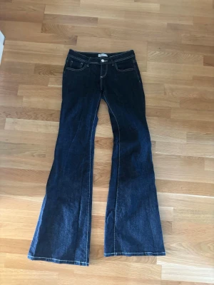 Marinblå bootcut jeans - Säljer mina lågmidjade marinblå jeans från ginatricot som inte säljs längre. Lappen där bak har sprungit lite men syns knappt. De är i storlek 36 tall och passar perfekt för mig som är 170