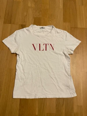 Valentino T-shirt  - Vit t-shirt med röd valentino-logga på bröstet som är riktig. Klassisk passform och rund hals. Tillverkad i mjuk bomull. Enkel och stilren design som passar till det mesta. Den har några hål (bild 4-5) som går att laga väldigt enkelt. Storlek xs