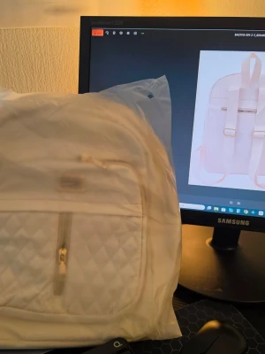 Ljusbeige quiltad ryggsäck - Snygg ljusbeige ryggsäck med quiltat mönster på framsidan och guldfärgade dragkedjor. Väskan har ett stort huvudfack, en framficka med dragkedja och justerbara axelband. Perfekt för dig som vill ha en stilren och trendig accessoar till skolan eller stan.